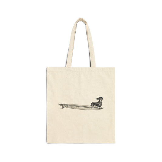 Beige canvas tote with a Dachshund dog on a long surfboard with racing flags on it. The dog has a checkered bandana around it's neck.