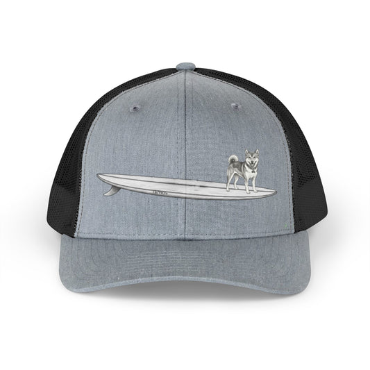 Gray and black mesh trucker hat with a graphic of a Shiba Inu dog hanging twenty on a long surfboard design on a gray background