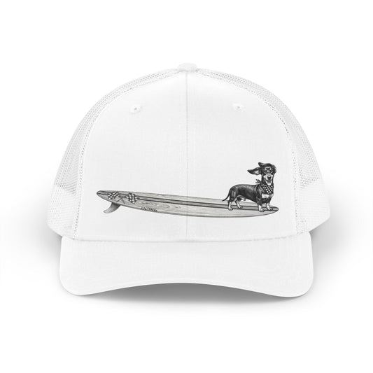 White mesh trucker hat with a Dachshund dog on a longboard surfboard with racing flags on it. The dog has a checkered bandana around it's neck.