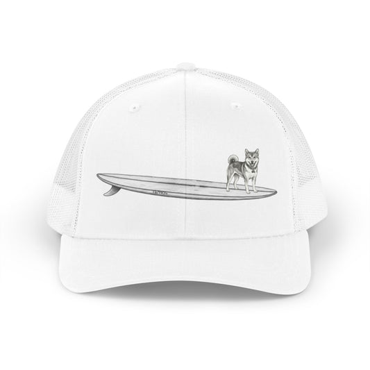 White mesh trucker hat with a graphic of a Shiba Inu dog hanging twenty on a long  surfboard design on a white background