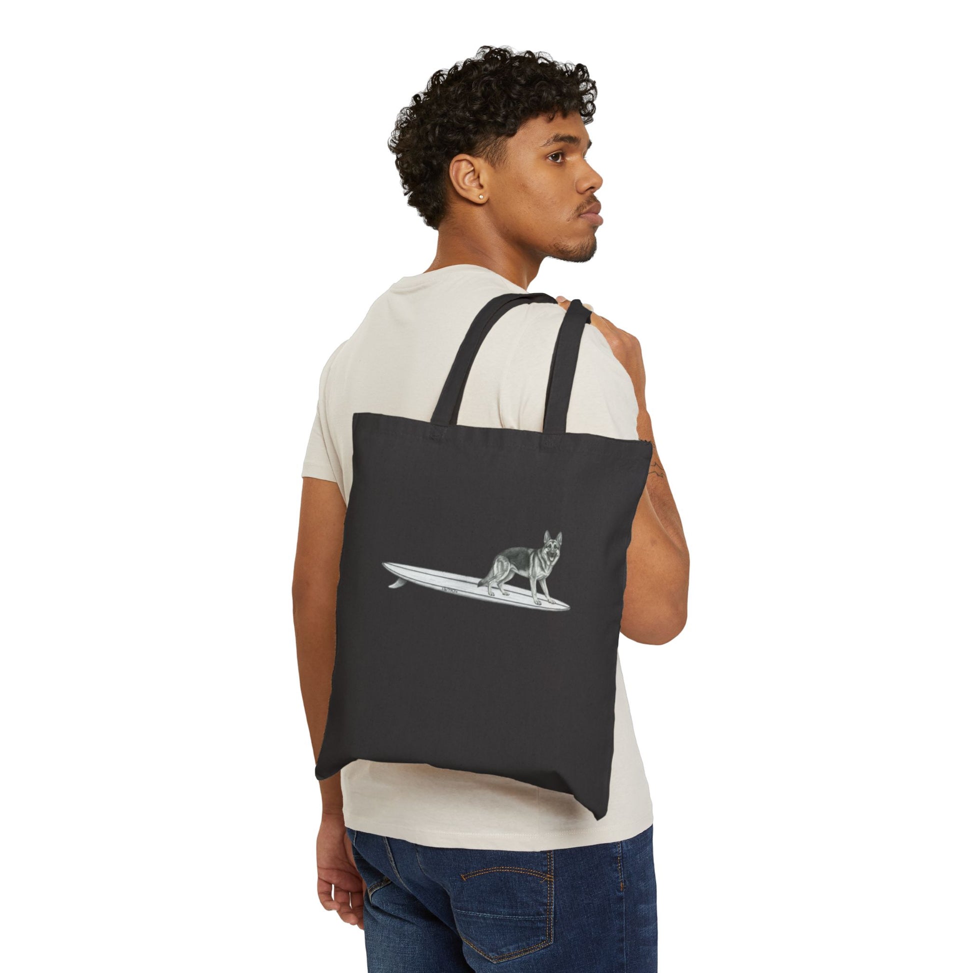 Man carrying a Black tote bag with a graphic of a German Shepherd dog hanging twenty on a long surfboard on a black background.