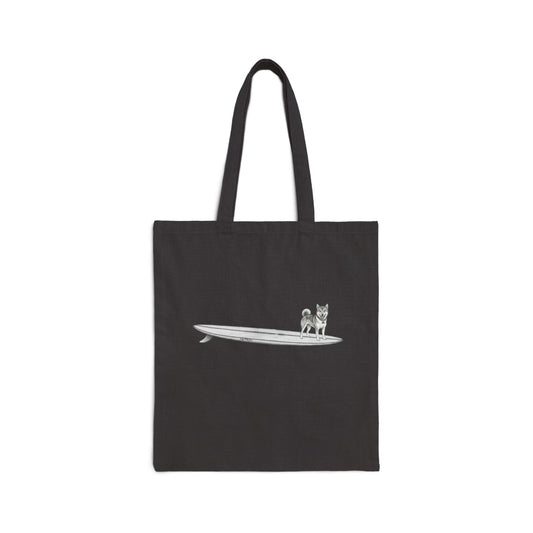 Black tote bag with a design of a Shiba Inu dog hanging twenty on a long surfboard on a black background