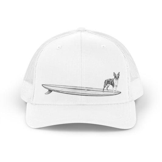 White trucker hat with a black and white graphic of a Boston Terrier on a surfboard design on a white background. 