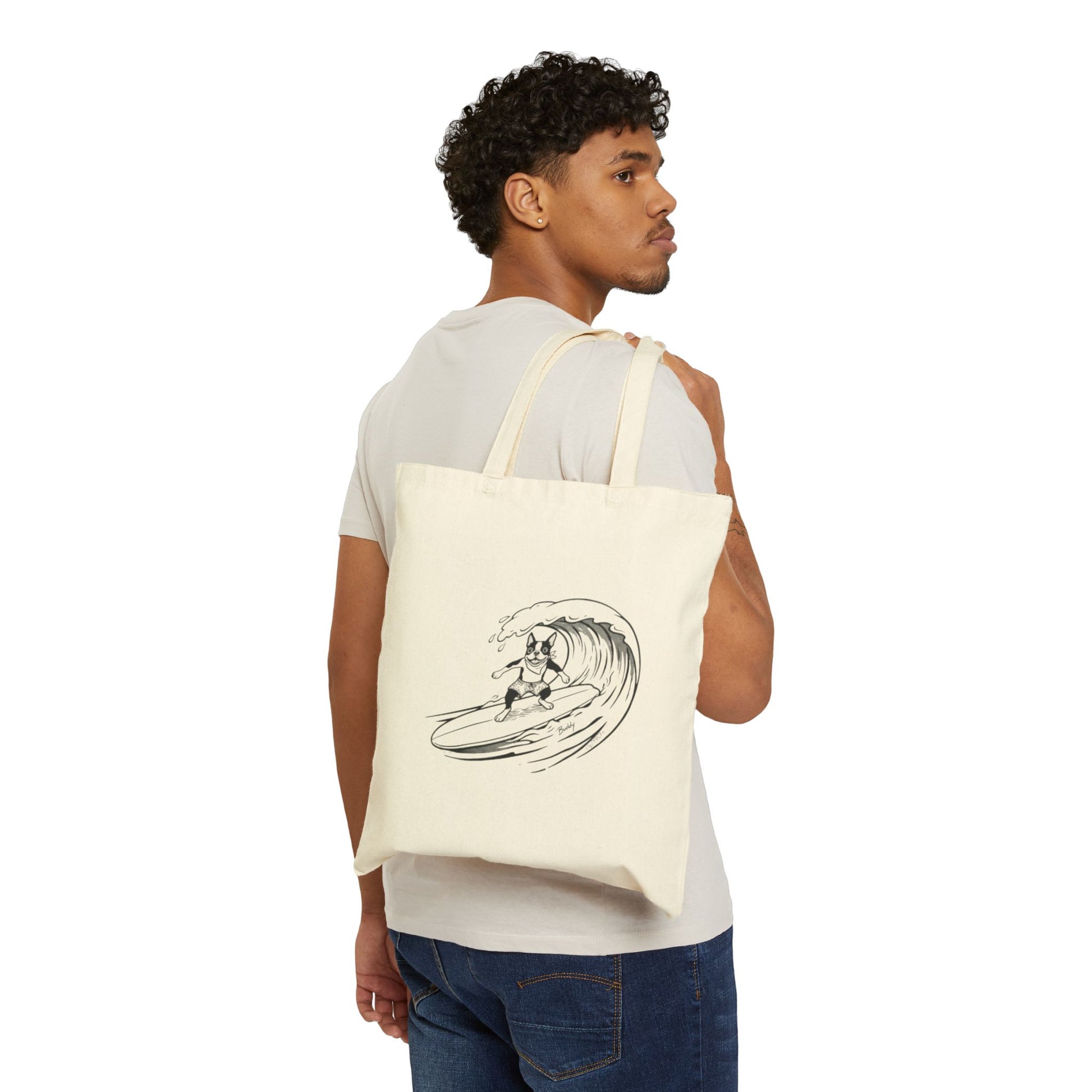Man carrying a Beige tote bag with a graphic of a boston terrier riding a big wave on a longboard with a beige background.