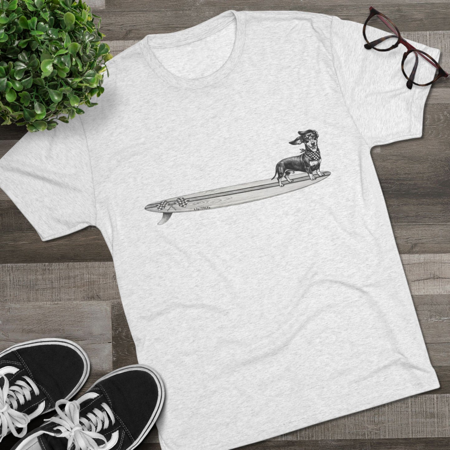 White tshirt with a Dachshund dog on a longboard surfboard with racing flags on it. The dog has a checkered bandana around it's neck. 