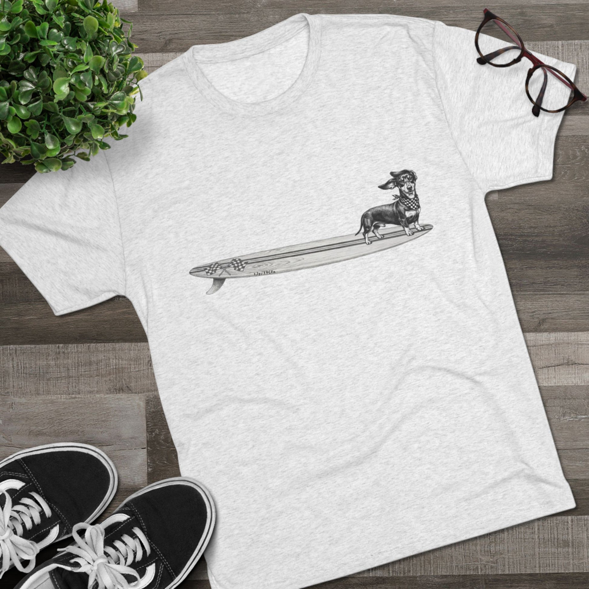 White tshirt with a Dachshund dog on a longboard surfboard with racing flags on it. The dog has a checkered bandana around it's neck. 