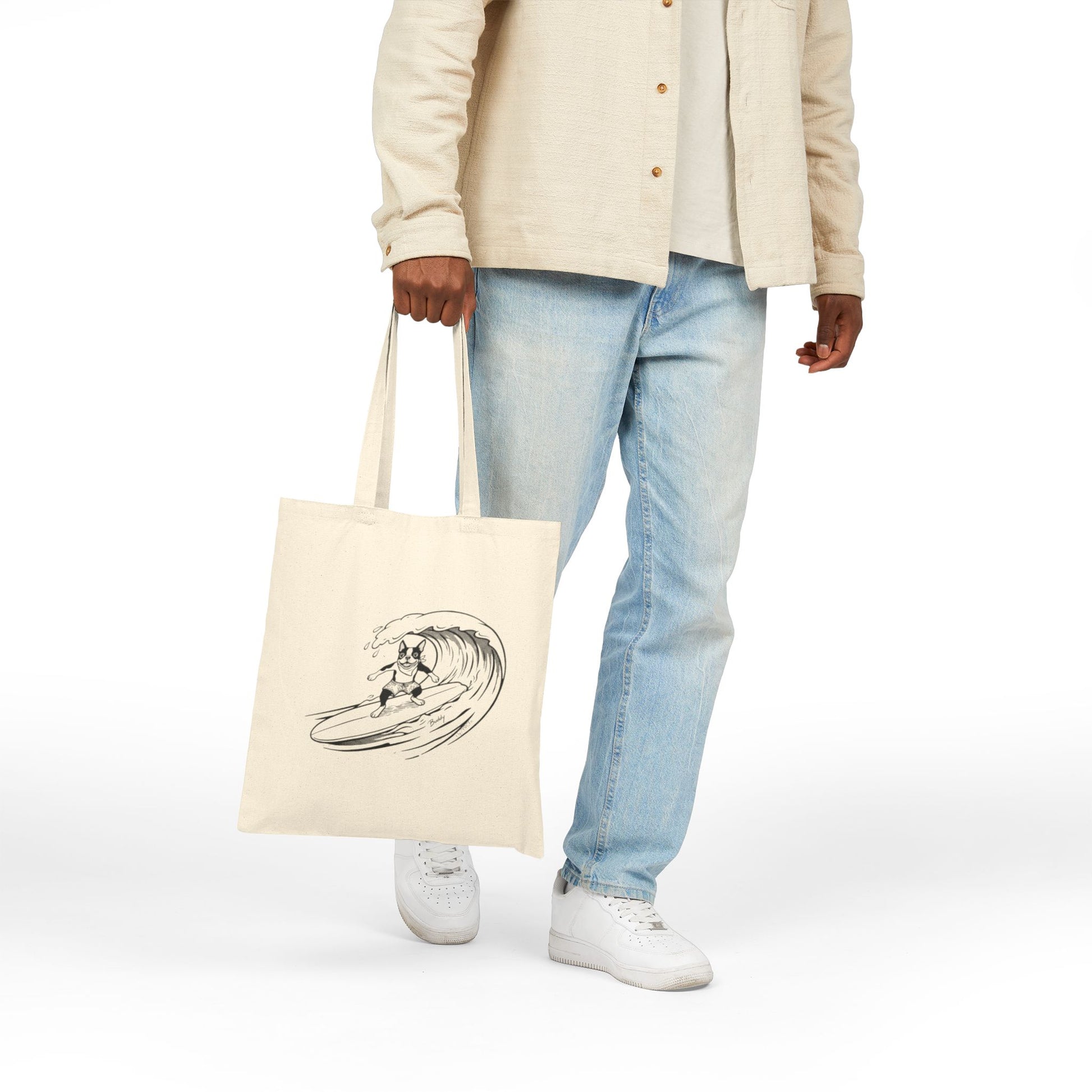 Person holding a Beige tote bag with a graphic of a boston terrier riding a big wave on a longboard with a beige background.