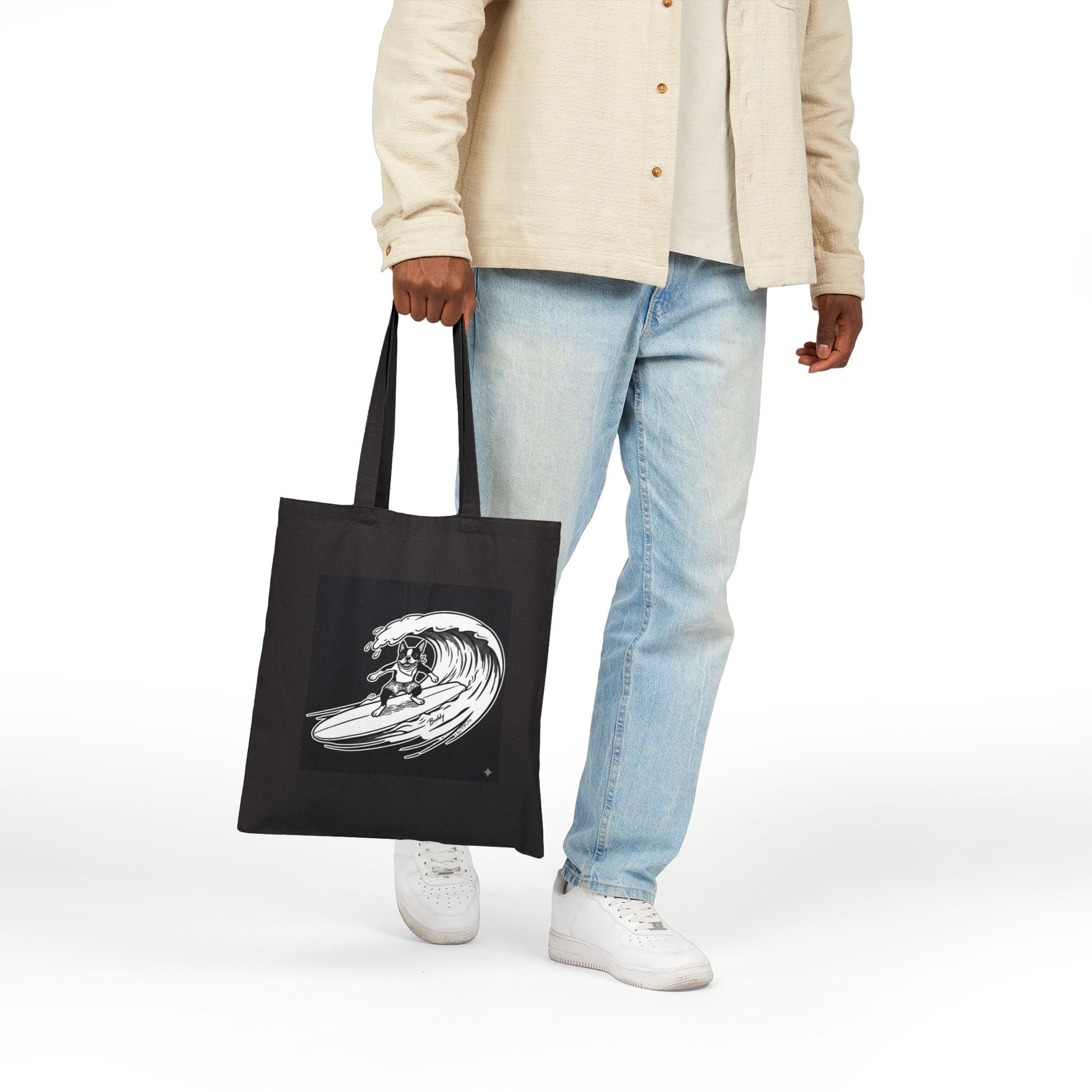 Person holding a Black tote bag with a graphic of a boston terrier riding a big wave on a longboard with a black background.