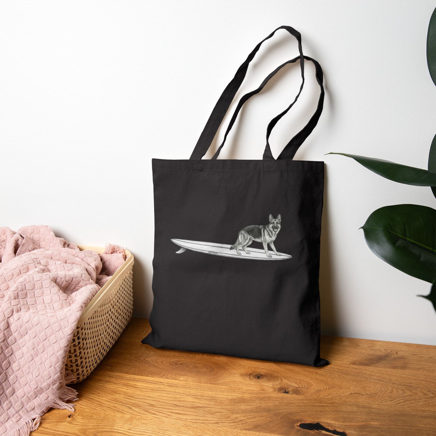 Black tote bag with a graphic of a German Shepherd dog hanging twenty on a long surfboard on a black background.