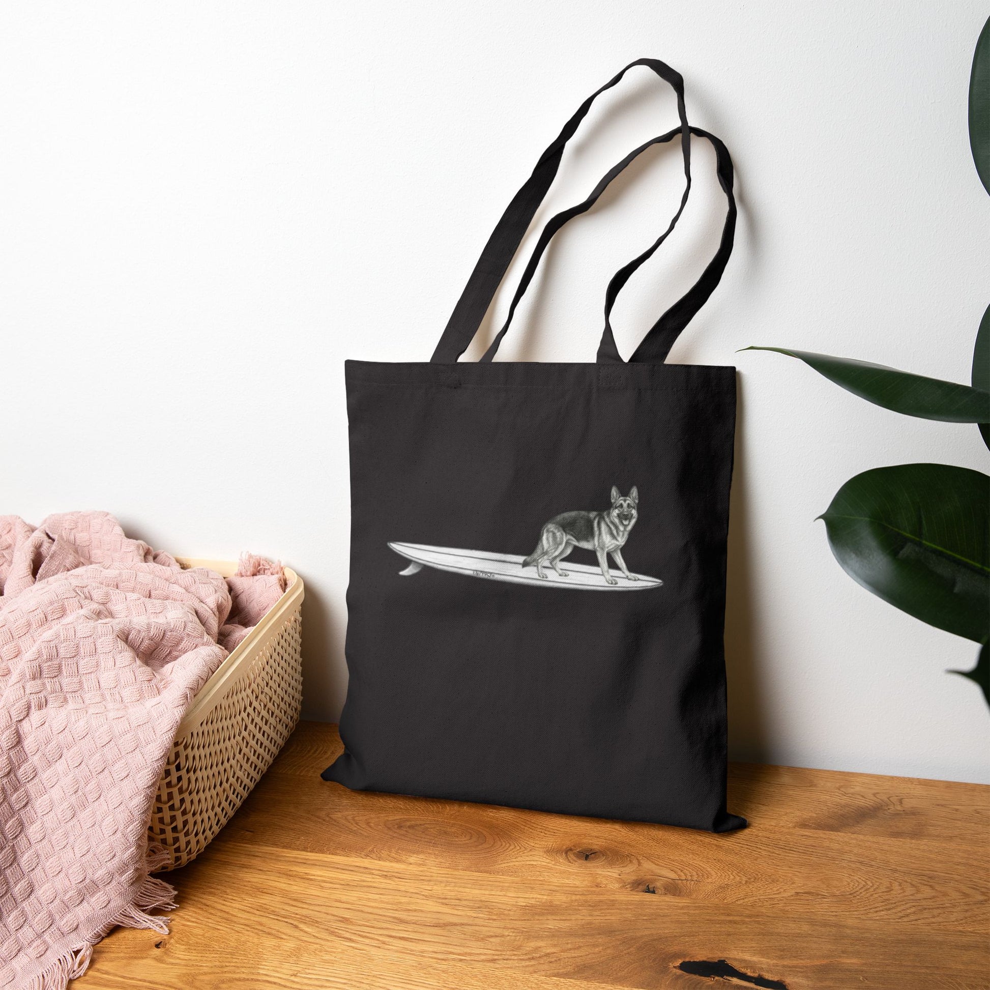 Black tote bag with a graphic of a German Shepherd dog hanging twenty on a long surfboard on a black background.