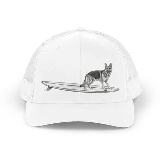 White mesh trucker hat with a graphic of a German Shepherd dog hanging twenty on a long surfboard on a white background.