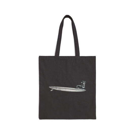 Black canvas tote with a Dachshund dog on a long surfboard with racing flags on it. The dog has a checkered bandana around it's neck.