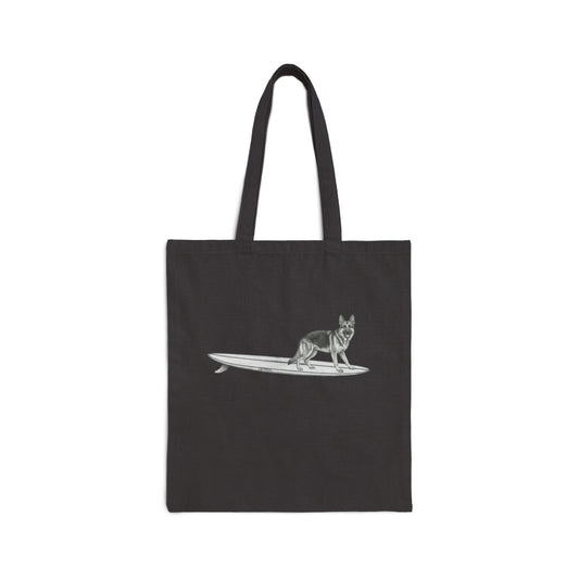 Black tote bag with a graphic of a German Shepherd dog hanging twenty on a long surfboard on a black background.