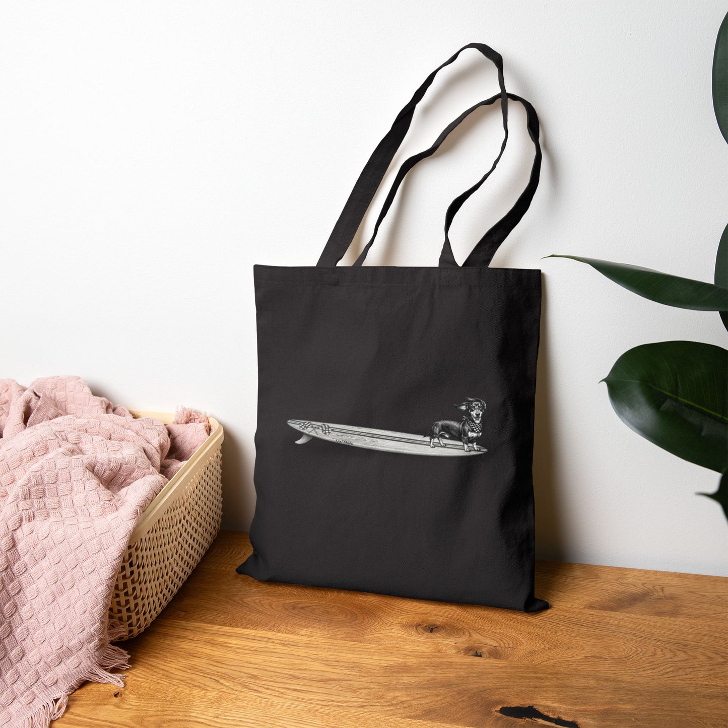 Black canvas tote with a Dachshund dog on a long surfboard with racing flags on it. The dog has a checkered bandana around it's neck.